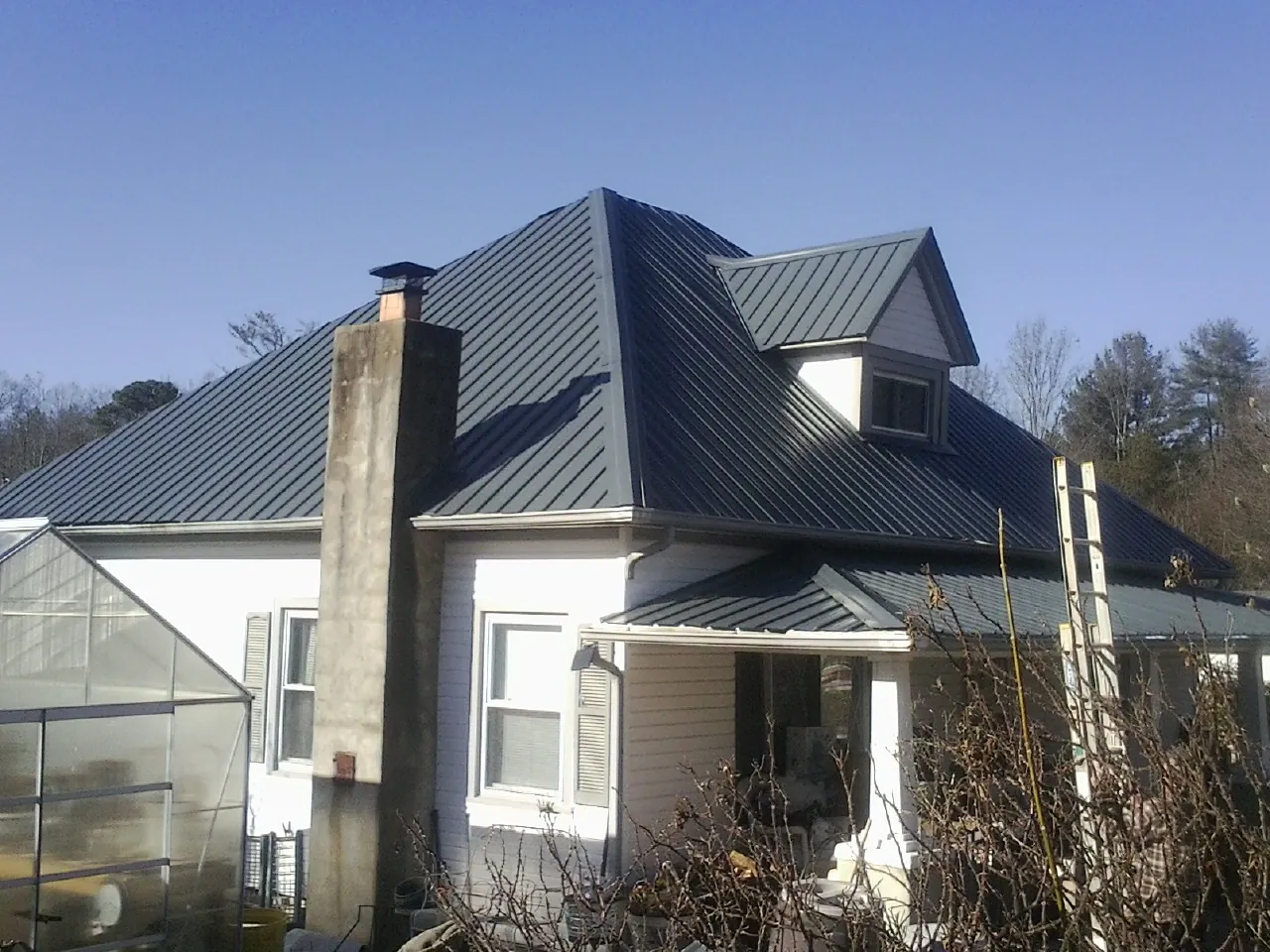 Dark blue standing seam metal roof on a white farmhouse with dormer — Slate & Tile Roof Repair by Roofing Brothers in North Smithfield