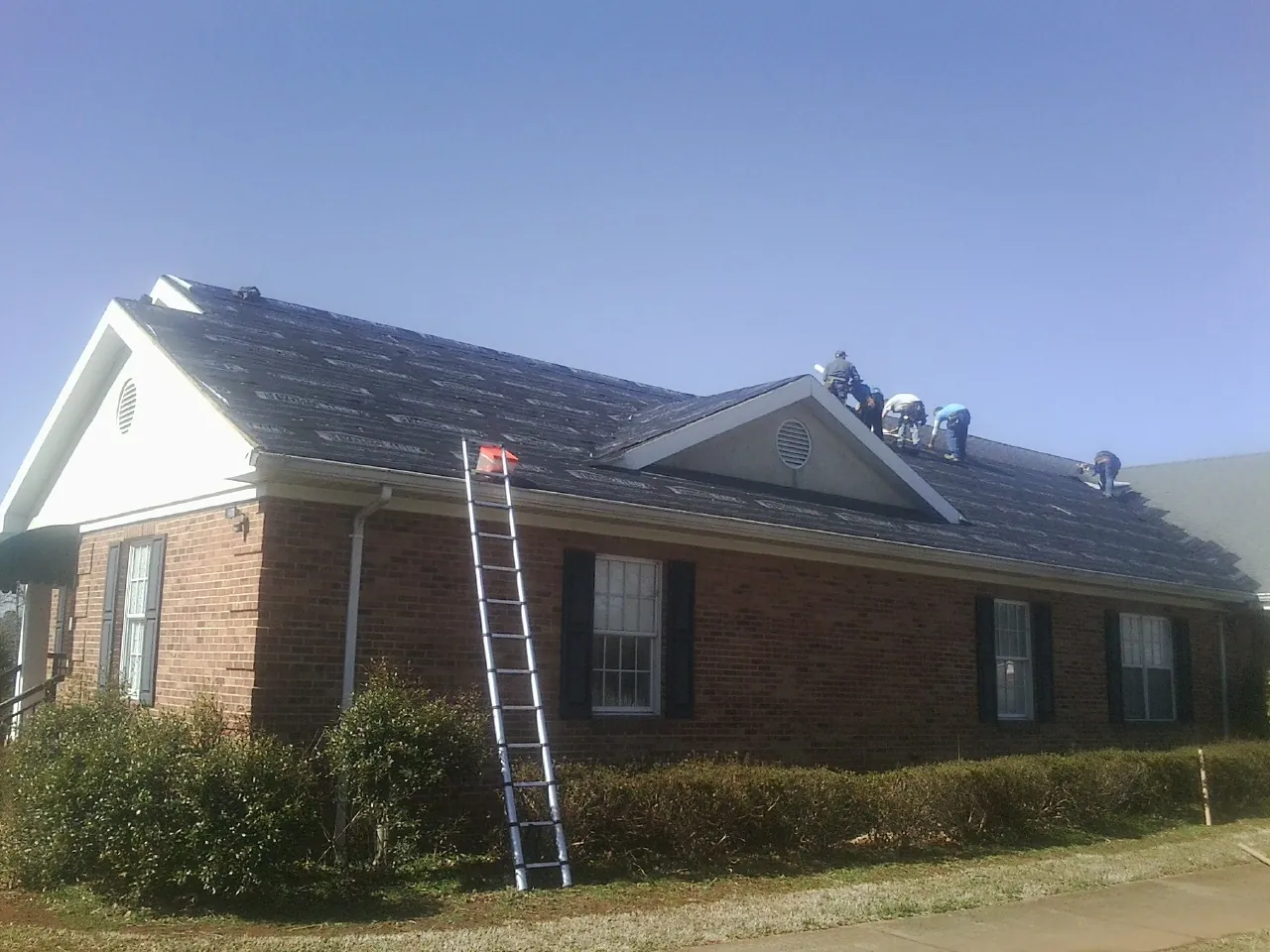 Crew tearing shingles off a brick ranch roof with a ladder set — Metal Roof Repair work by our crew in North Smithfield