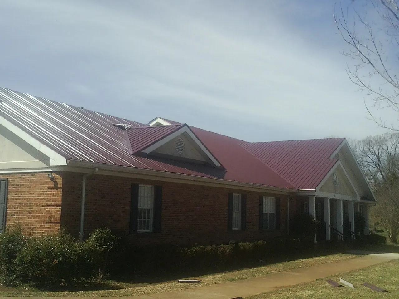 Red metal roof with gabled entries on a long brick building, from a Hail Damage Roof Repair job in North Smithfield