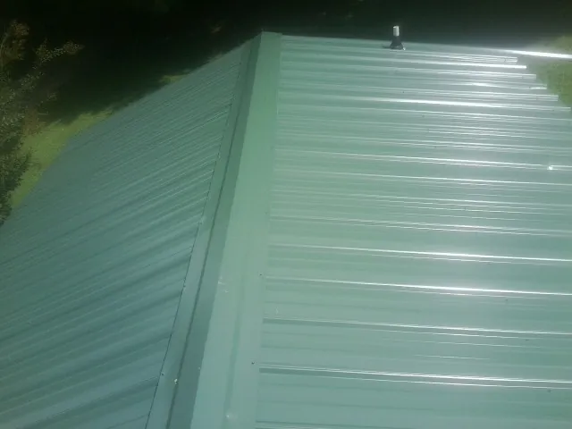 New green metal panels meeting at the ridge of a roof — Flat Roof Repair work by our crew in North Smithfield