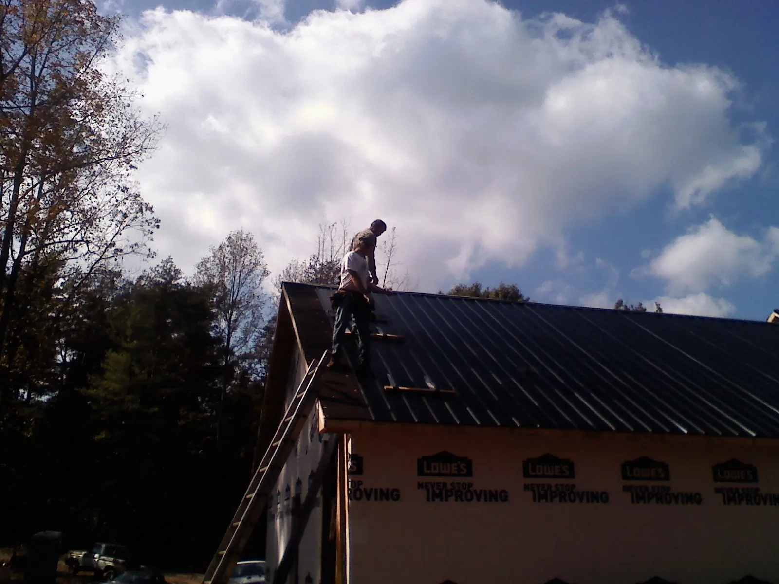 Roofer fastening dark metal panels high against a cloudy sky, from a Roof Inspection job in North Smithfield