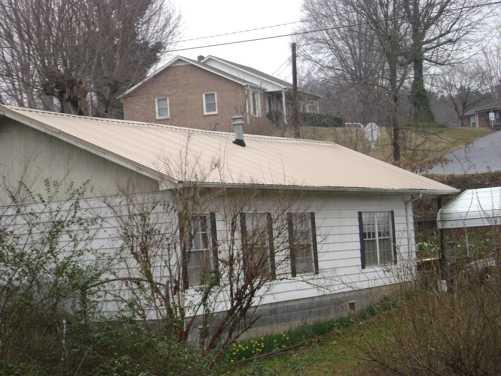 Tan metal roof on a white sided house set into a hillside — Commercial Roofing by Roofing Brothers in North Smithfield