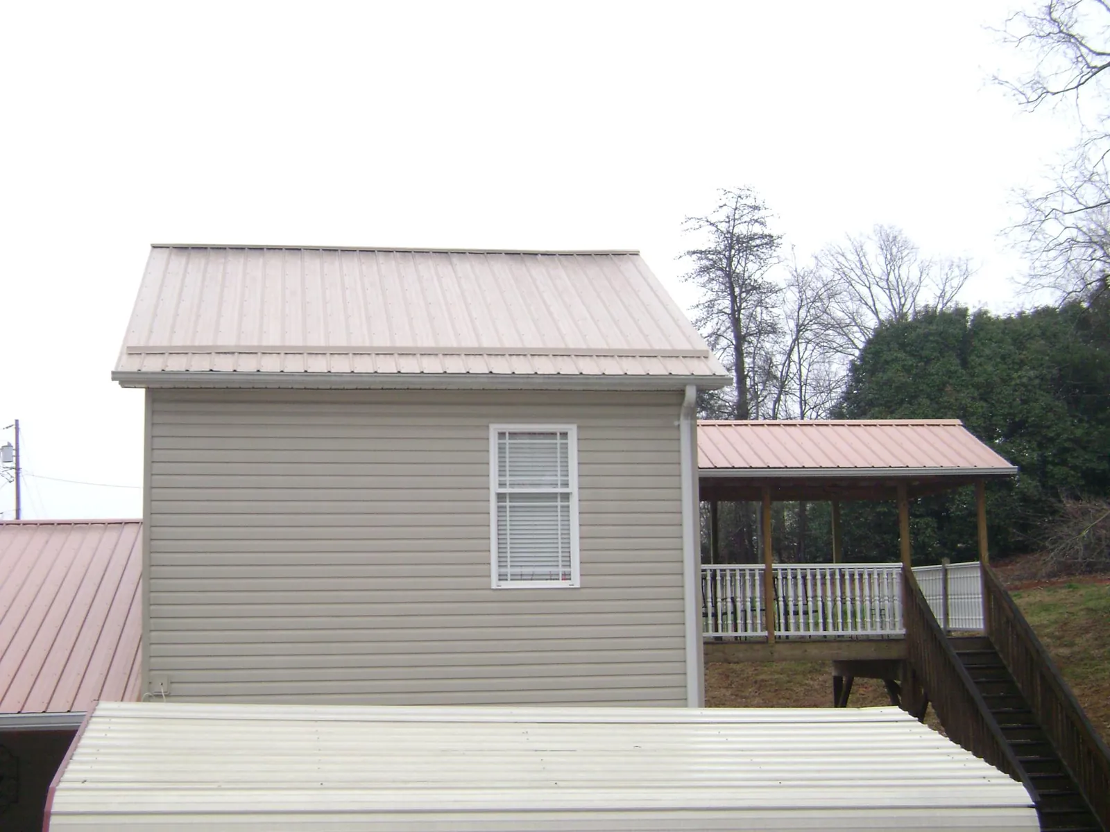 Tan metal roofs on a two story addition and attached porch, from a Roof Replacement job in North Smithfield
